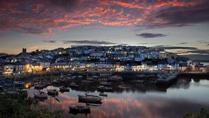 A coastal town at dusk with buildings along the waterfront and boats docked in the harbor.