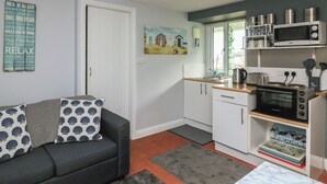 A compact living space with a kitchenette, a sofa with patterned cushions, a painting on the wall, and a door leading to another room.