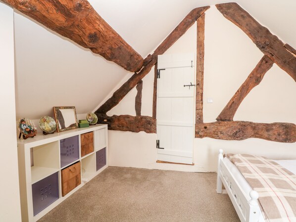 A room with exposed wooden beams, a white door, a white bed, and a white built-in storage unit with multiple compartments. - Chapel Cottage (Tarporley)