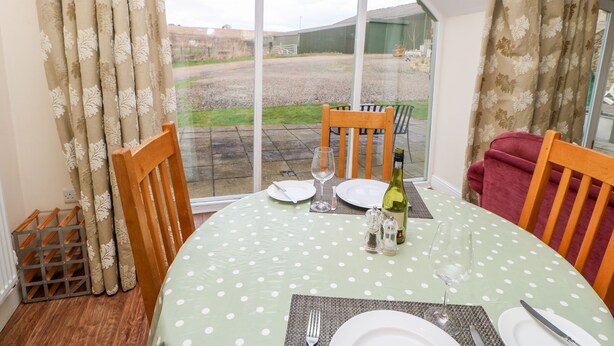 A dining area with a table set for two, featuring a polka dot tablecloth, wooden chairs, and a view through a large arched window. - Bowes Barn (Gateshead)