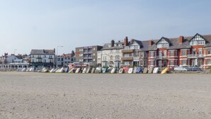 A coastal town with a row of terraced houses and a sandy beach in the foreground. - The Yatt (Colwyn Bay)