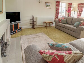 A living room with a sofa, a television, a radiator, and a window with curtains. - The Yatt (Colwyn Bay)