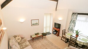 A living room with a sofa, a small table, a TV stand, and a dining area with a table and chairs. - The Old Coach House (Penmaenmawr)