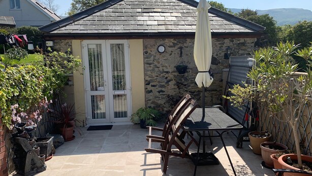 A stone house with a tiled patio, a table with chairs, and potted plants. - The Old Coach House (Penmaenmawr)