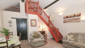 A cozy living room with a wooden staircase, a dining area with a table and chairs, and a sofa. - The Old Coach House (Penmaenmawr)