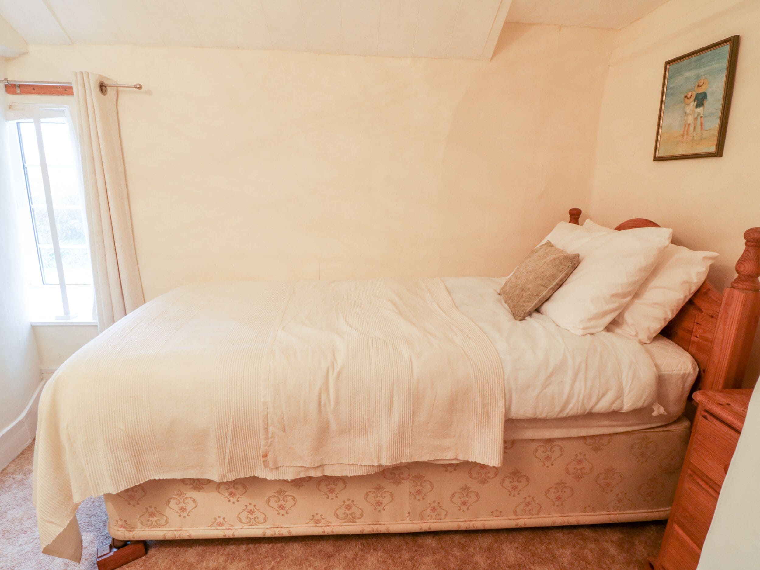 A single bed with a patterned mattress, a wooden headboard, and a bedside table with a lamp.