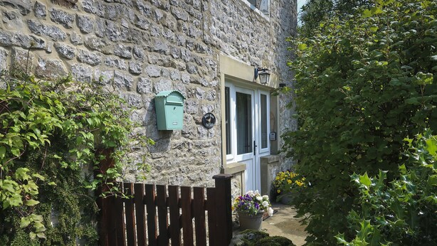 Ein Steinhaus mit einem Holztor, einer kleinen Veranda und einem Schild, das auf ein Ferienhaus hinweist.