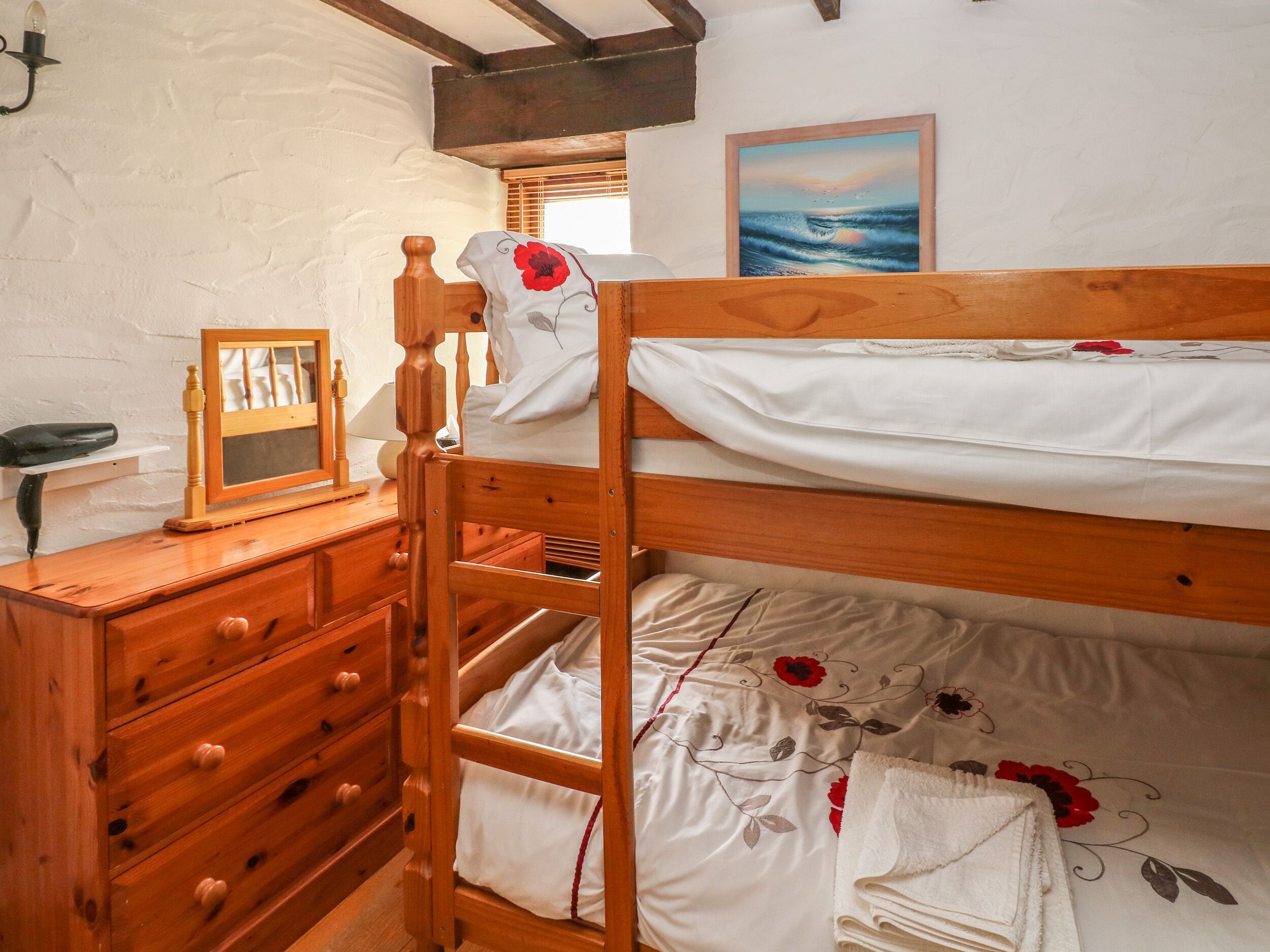 A bunk bed with a wooden frame, a bedside table with a lamp, a dresser with drawers, and a painting on the wall.