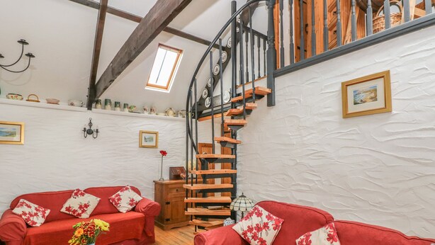 Una sala de estar acogedora con sofás rojos, una mesa de centro de madera, una escalera de madera y una pared blanca con textura.