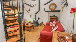 Un interior rústico con una escalera de madera, un sofá rojo, una mesa de madera con un plato y un reloj antiguo en la pared.