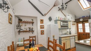 Una cocina rústica con muebles de madera, una mesa de comedor y un frutero, además de un refrigerador pequeño.