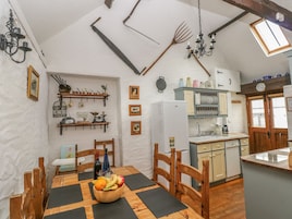 Una cocina rústica con muebles de madera, una mesa de comedor y un frutero, además de un refrigerador pequeño.
