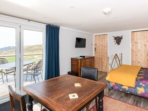 A room with a wooden table, a bed with a floral bedspread, a desk with a chair, and a view of the outdoors through a sliding glass door. - Haka Lodge (Aberystwyth)
