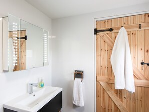 A modern bathroom with a white vanity, a large mirror with lights, a wooden door, and a towel rack. - Haka Lodge (Aberystwyth)