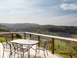 A deck with a table and chairs overlooking a valley with hills and a clear sky.