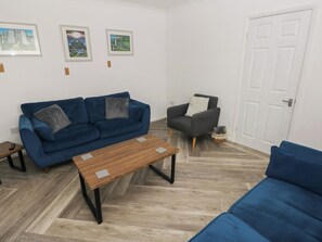 A living room with a blue sofa, a wooden coffee table, a grey armchair, and a white door. There are three framed pictures on the wall. - Cwtch Ar Y Mor (Burry Port)