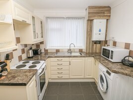 A compact kitchen with a stove, microwave, sink, and a washing machine.