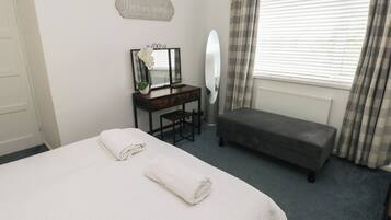 Un dormitorio con una cama, un escritorio con espejo, un banco y un cartel que dice 'Be our guest'.