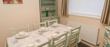 A dining room with a table set for six, surrounded by chairs, a green cabinet with glassware, and a window with curtains.