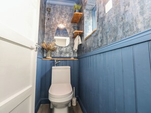 A bathroom with a toilet, a mirror, a shelf with a plant, and a towel hanging on the wall. - Cwtch Ar Y Mor (Burry Port)