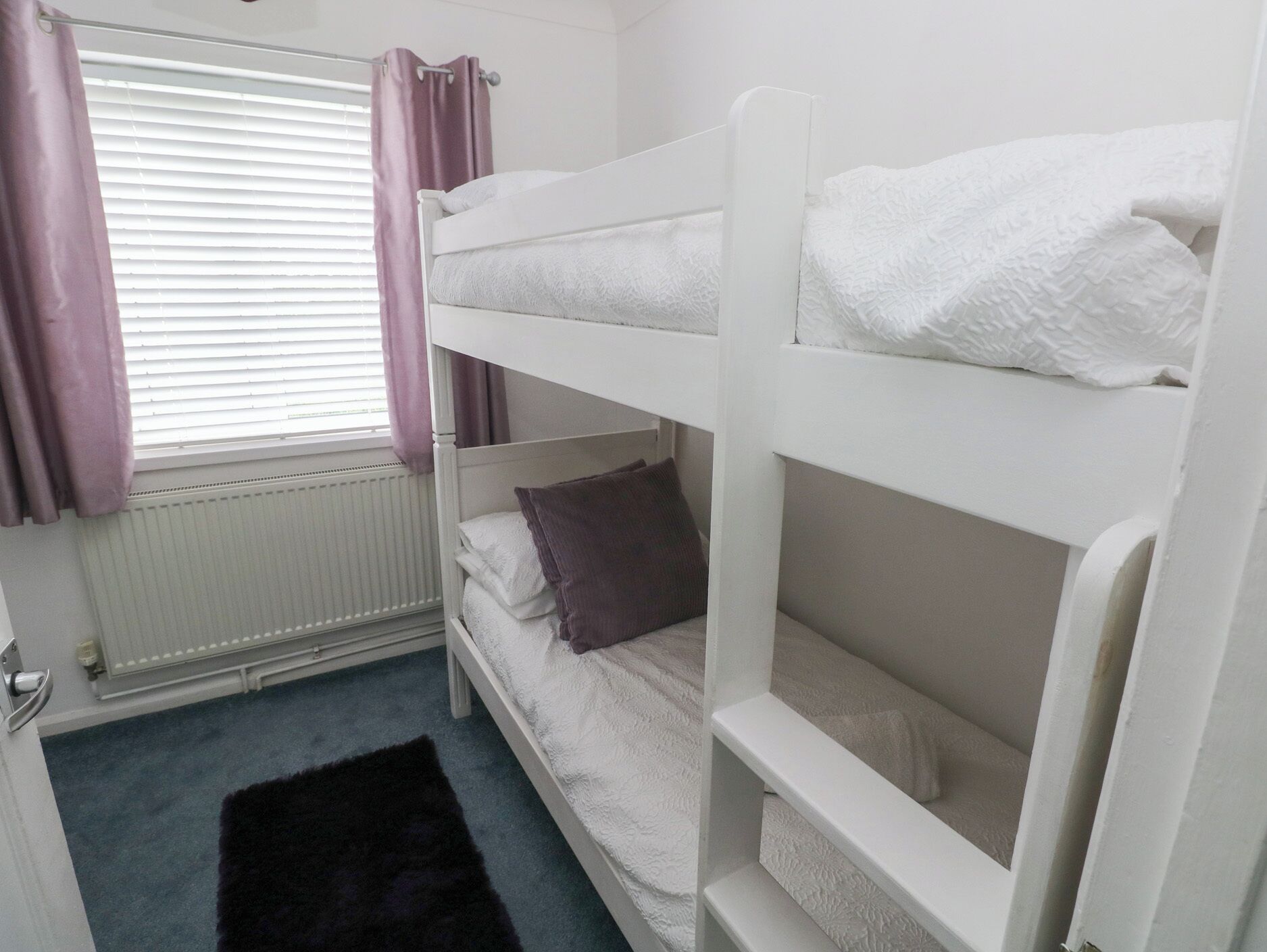 A bunk bed room with a window, curtains, and a radiator.