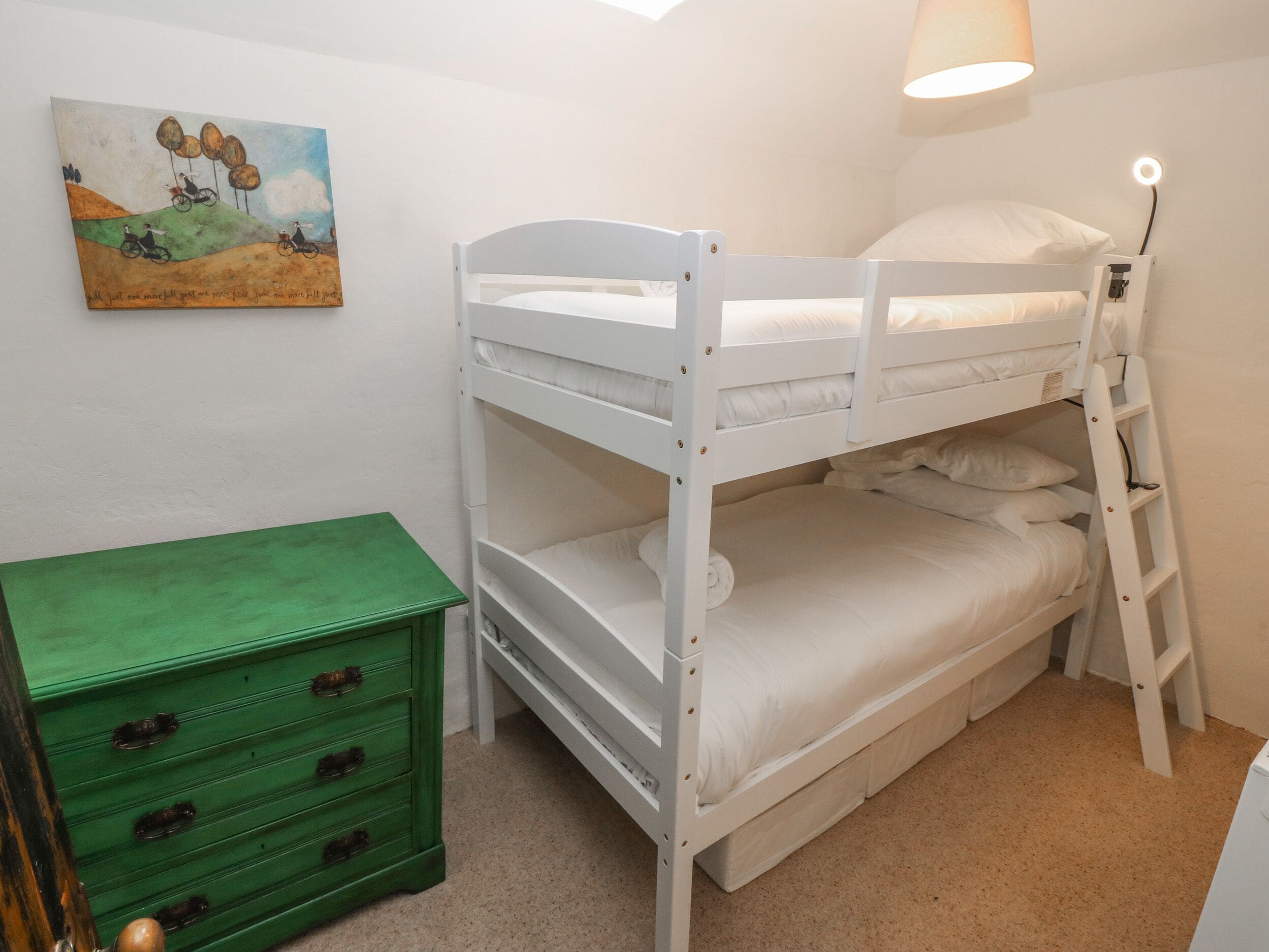 Un lit superposé avec une échelle, une commode verte et un tableau accroché au mur.