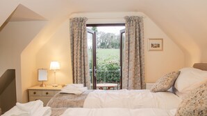 A bedroom with a bed, a nightstand, a lamp, a window with curtains, and a view of a garden.
