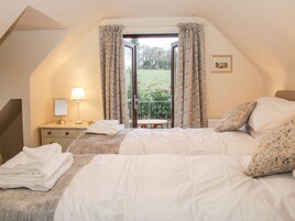Un dormitorio con cama, mesita de noche, lámpara, ventana con cortinas y vista a un jardín.