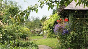 A garden pathway leading to a wooden structure surrounded by lush greenery and various flowering plants.