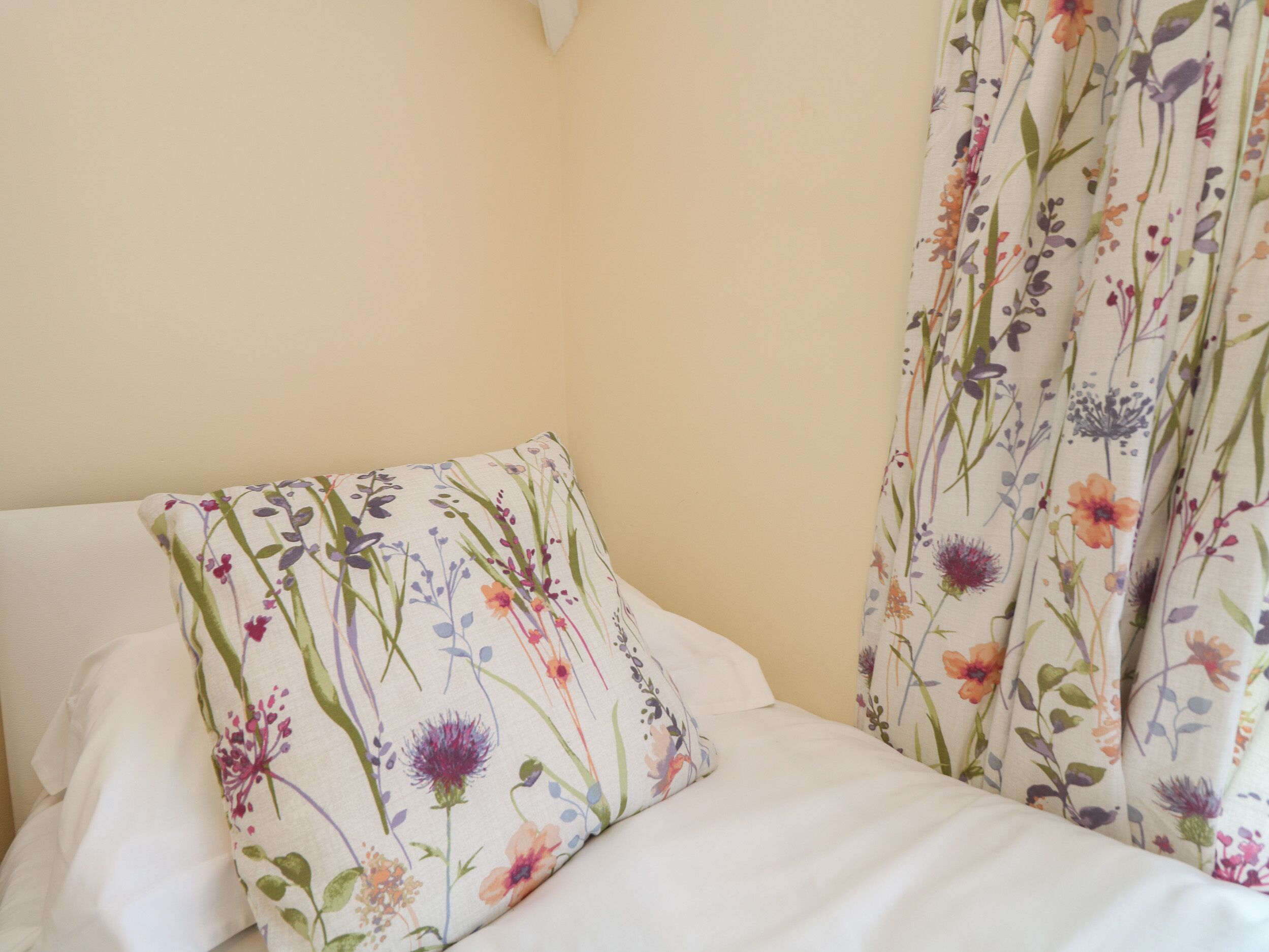 A bed with white bedding and a floral-patterned pillow and curtains.