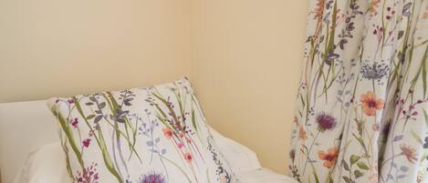 A bed with white bedding and a floral-patterned pillow and curtains.