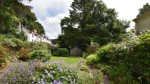 Un jardin où l’on trouve une grande variété de plantes et de fleurs, une clôture en bois et un abri de jardin en arrière-plan.