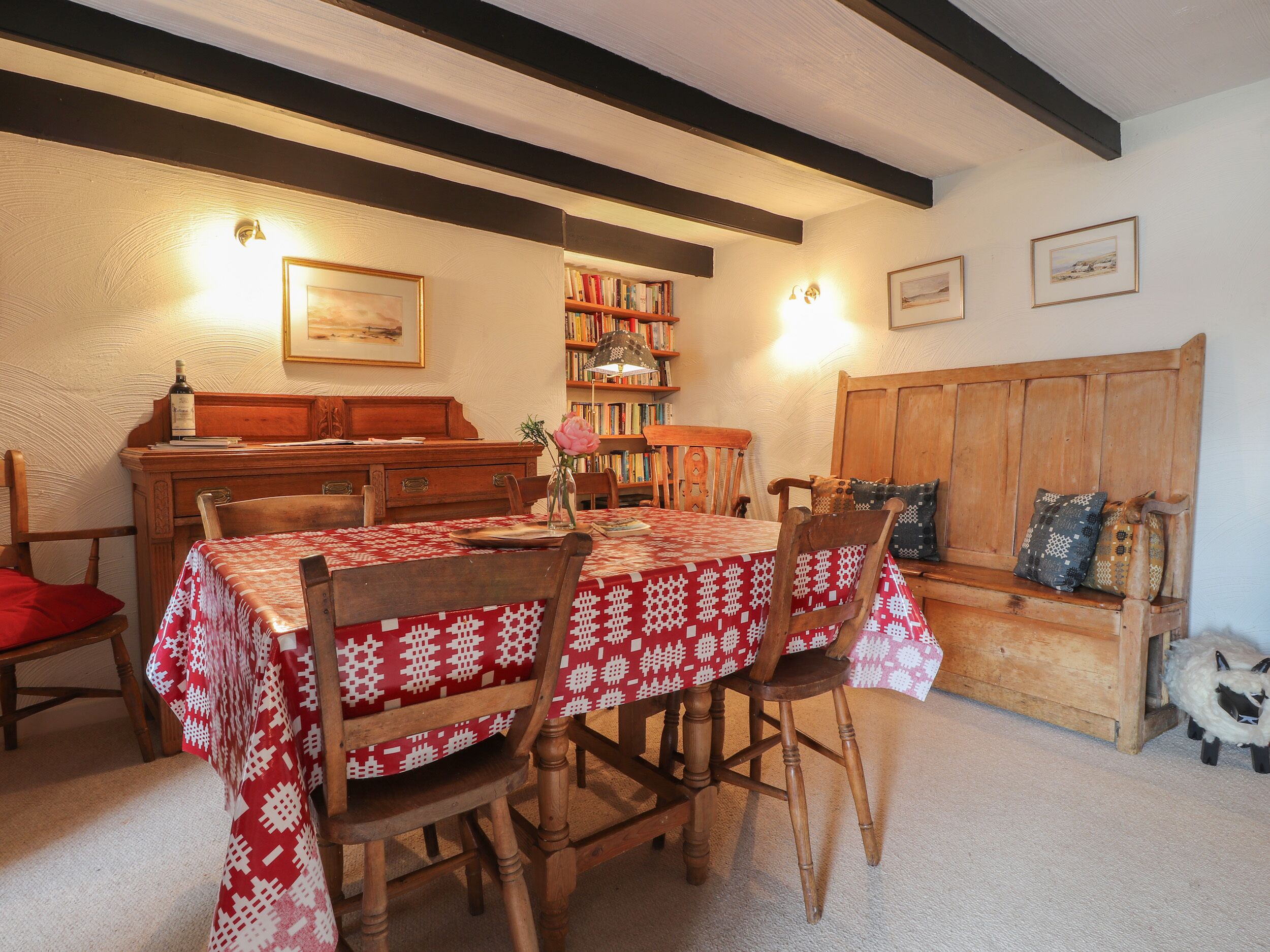 A dining area with a wooden table and chairs, a bookshelf, and a bench with cushions.