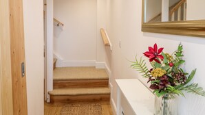 Un pasillo con una puerta de madera, una escalera y una consola blanca con un jarrón de flores.