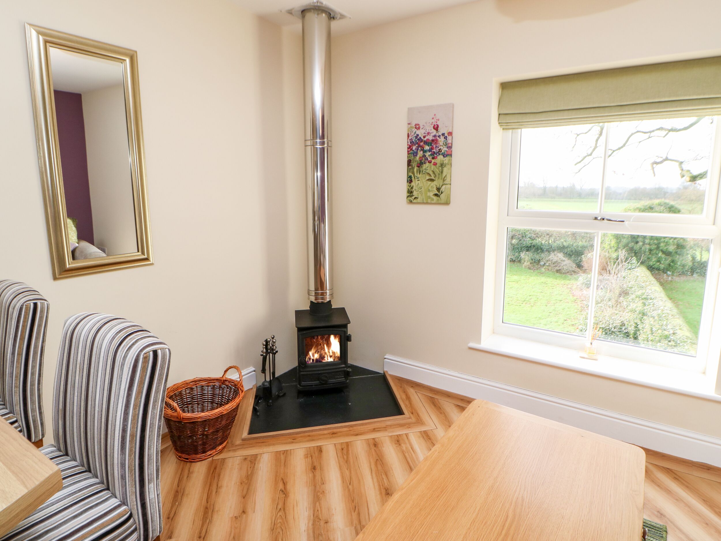 A cozy room with a wood-burning stove, a window with a view of the outdoors, a mirror, and striped furniture.