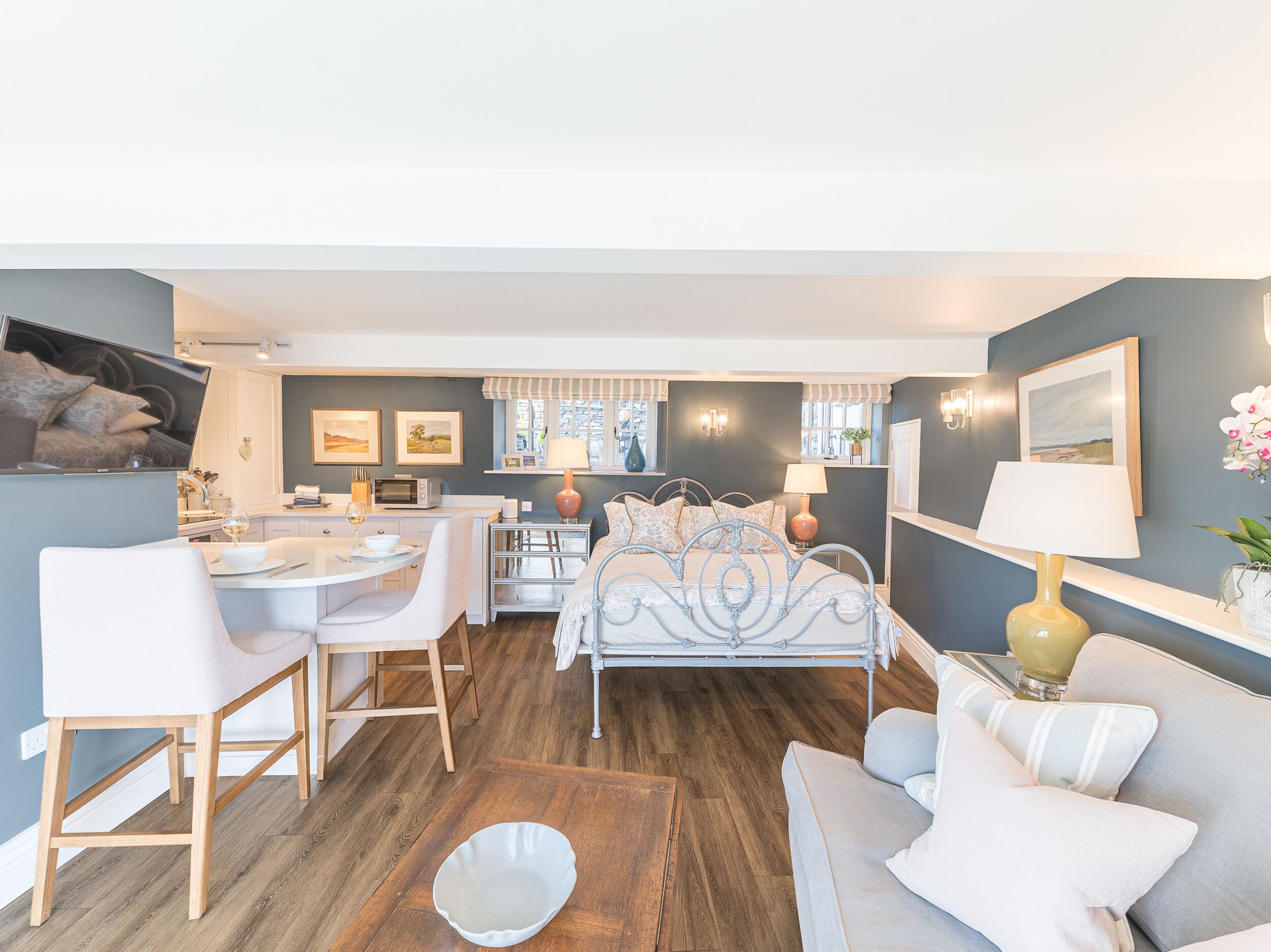A modern living room with a white sofa, a dining area with a white table, and a bed with a metal frame.