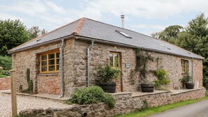 A stone building with a tiled roof, two windows, and potted plants. - The Old Haybarn (Newton Abbot)