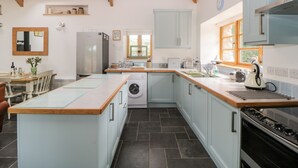 A modern kitchen with a central island, built-in appliances, and a large window providing natural light. - The Old Haybarn (Newton Abbot)