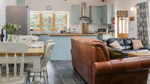 A spacious kitchen with a dining area, featuring a wooden ceiling, a built-in stove, and a large window. - The Old Haybarn (Newton Abbot)