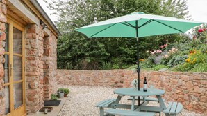 A stone building with a wooden door and windows, a gravel patio, a green picnic table with benches, and a green umbrella. - The Old Haybarn (Newton Abbot)