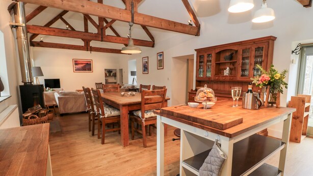 A spacious kitchen with wooden beams, a dining area, and a view of the living room. - The Old Workshop (Belford)