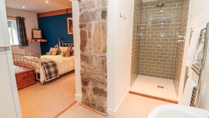 A bedroom with a bed, a nightstand, and a dresser. There is a bathroom with a shower and a bathtub. - The Old Workshop (Belford)