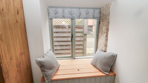 A cozy nook with a wooden bench and two pillows, a window with shutters, and a view of a wooden fence and building outside. - The Old Workshop (Belford)