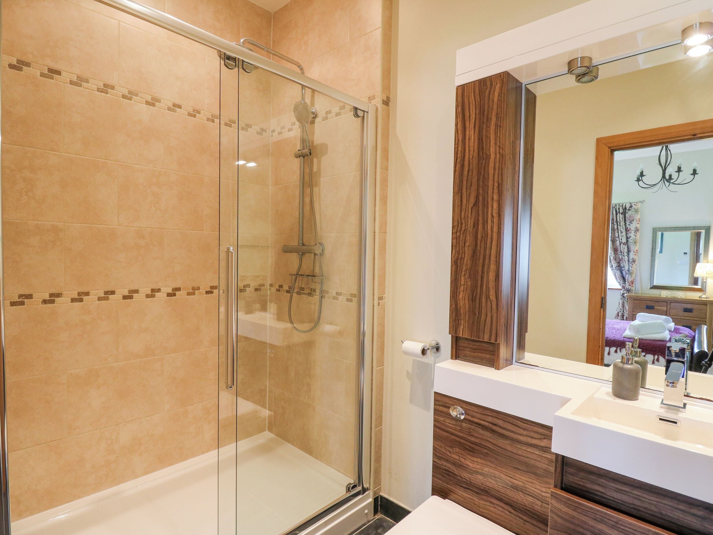 Un baño moderno con ducha envuelta en vidrio, tocador de madera y un espejo grande.