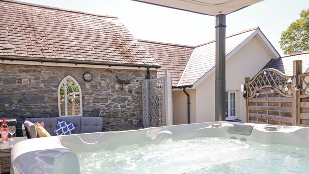 A hot tub in a backyard with stone walls and a wooden fence. - Yr Hen Beudy (Aberystwyth)