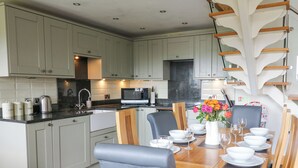 A modern kitchen with grey cabinets, a black countertop, and a dining area with a wooden table set for four. - Yr Hen Beudy (Aberystwyth)
