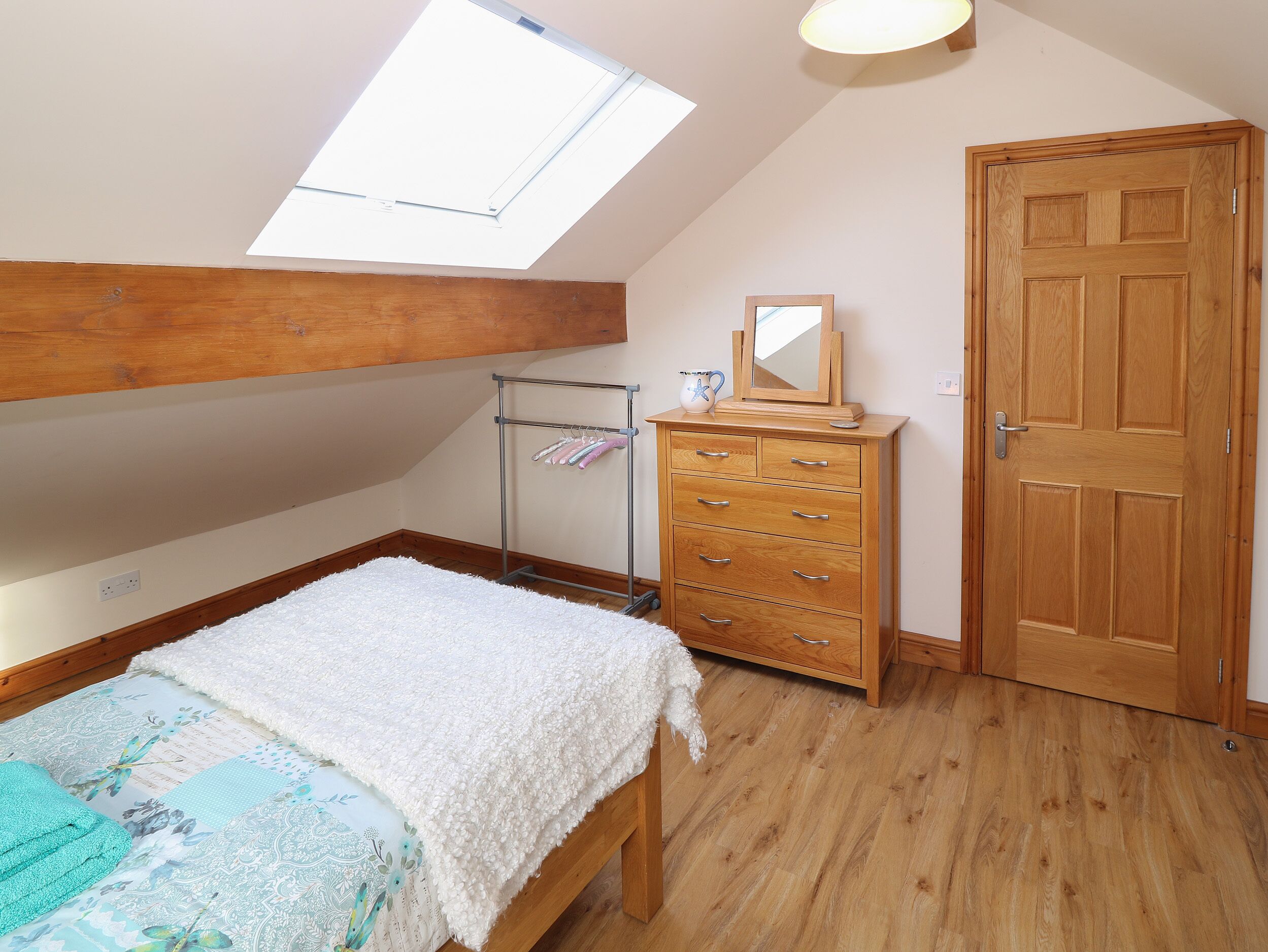 A bedroom with a skylight, wooden dresser, and a bed with a floral bedspread.