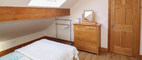 A bedroom with a skylight, wooden dresser, and a bed with a floral bedspread.