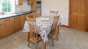 A kitchen with wooden cabinets, a microwave, and a dining table with chairs. - Bryn Eiddon (Pwllheli)