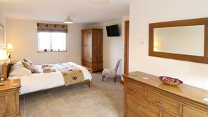 A bedroom with a bed, a wooden dresser, a chair, a television, and a window with a curtain. - Bryn Eiddon (Pwllheli)